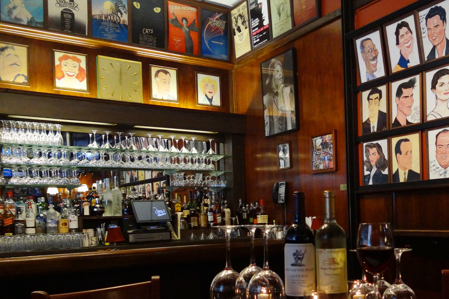 Corner of Sardi's bar showing caricatures on the wall, glasses lining the mirrored wall and wine bottles