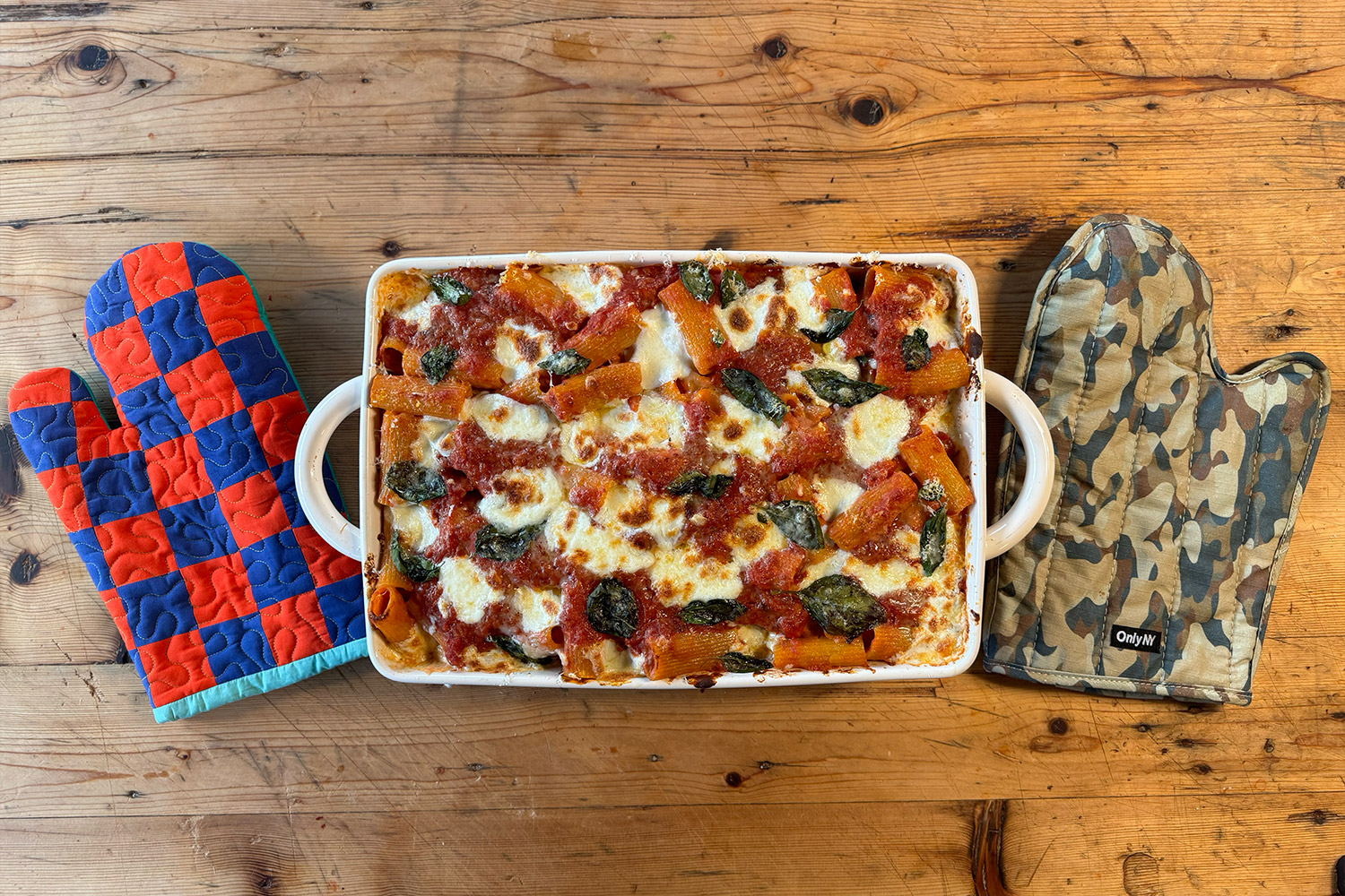 Baked Ziti from above with a checkered oven glove and camo oven glove