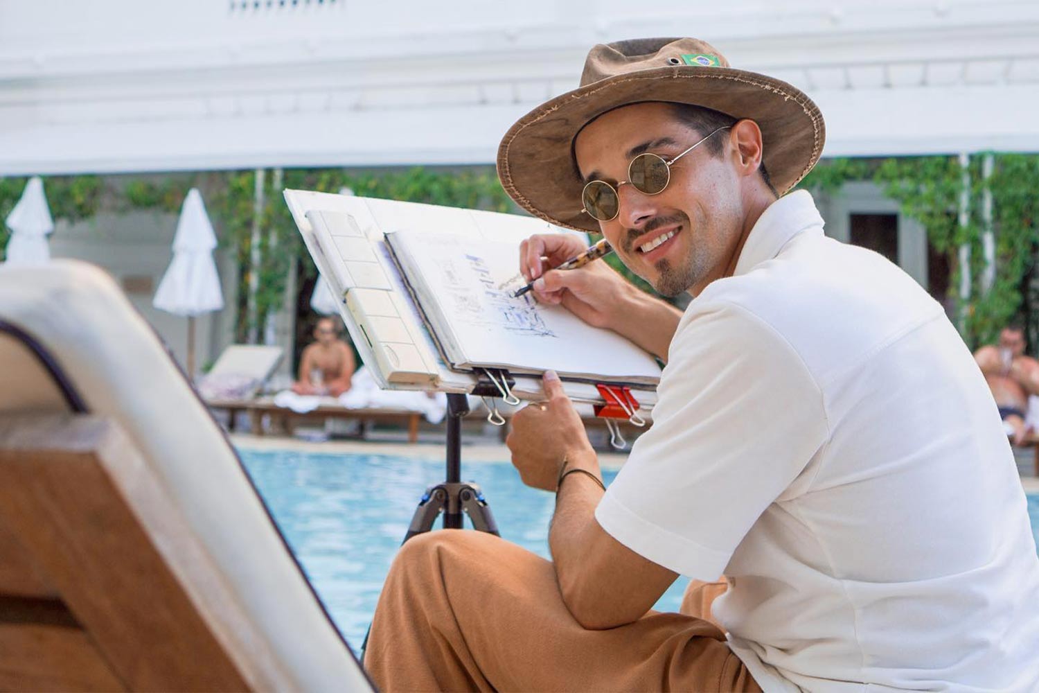 Artist, Alán Ramiro Manning, sketches in shades and a hat by the pool
