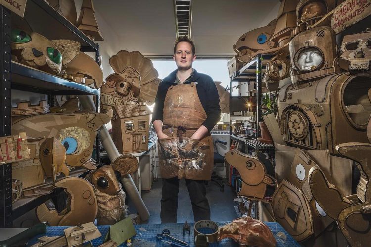 Man stands in workshop full of wearable cardboard art and costumes
