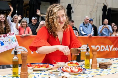Woman in outside red dress with curly hair making a tomato dish on the Today Show in front of crowd