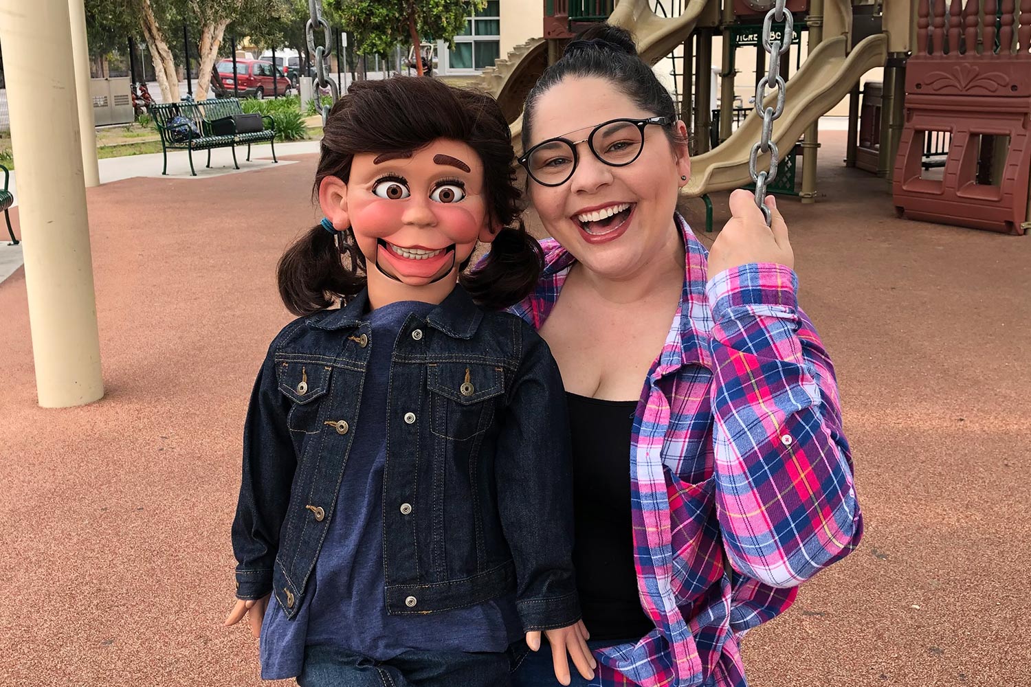 Woman poses on a playground swing with with a ventriloquist doll