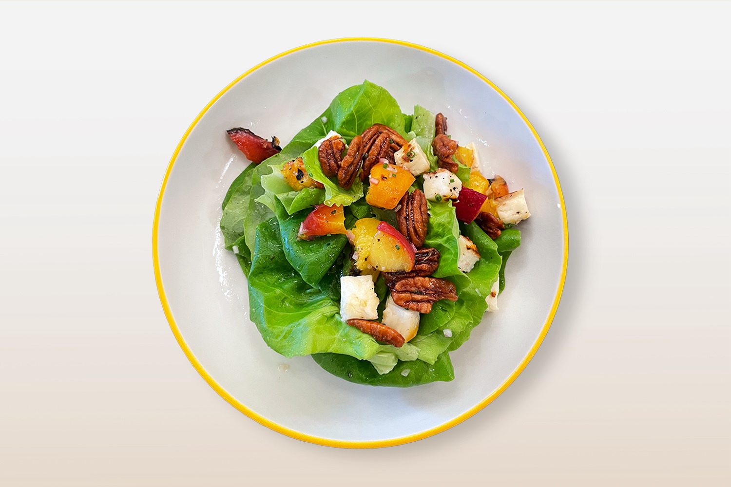 Multi-colored salad on a white plate with a yellow trim against a neutral gradient background