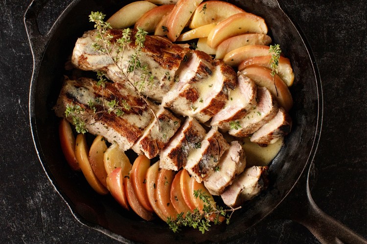 Apple and pork dish in a skillet on a black background